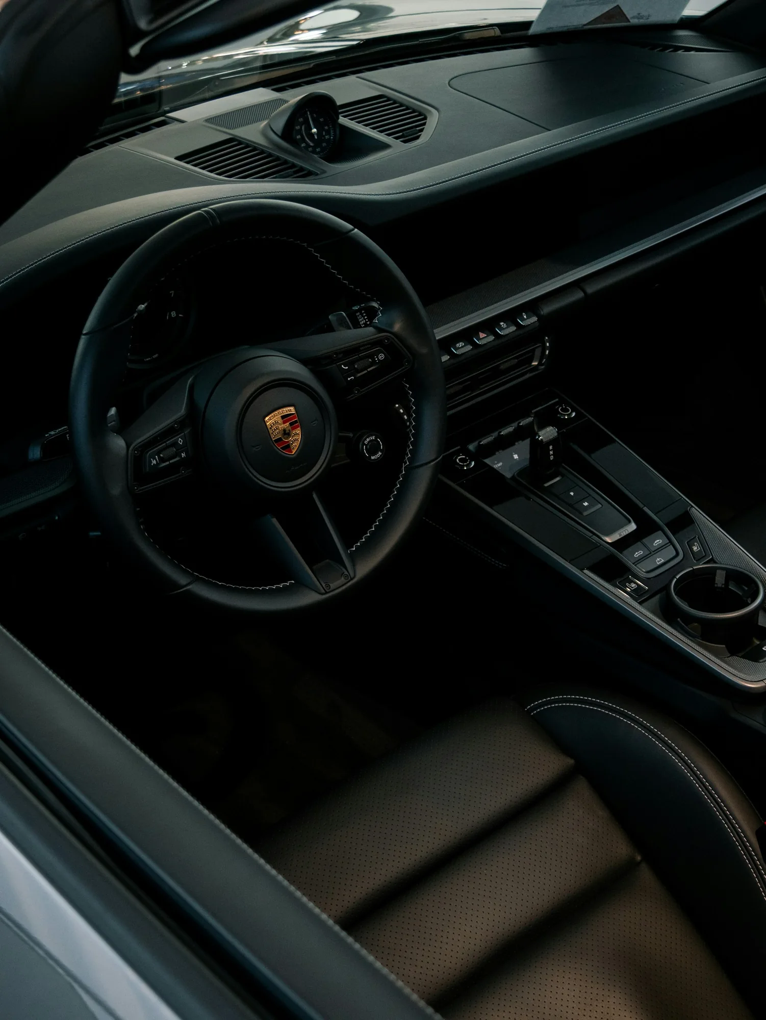 Intérieur Porsche en cuir noir, vu depuis la porte conducteur ouverte vers le volant et le tableau de bord